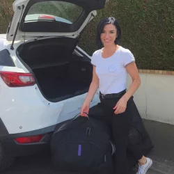 Praticienne d’Accent Massage transportant son matériel devant un véhicule avec le coffre ouvert.